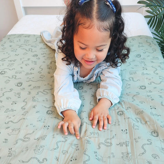 Child playing on a bed with a patterned sheet. Bedwetting Brolly Sheets - Animal Kingdom