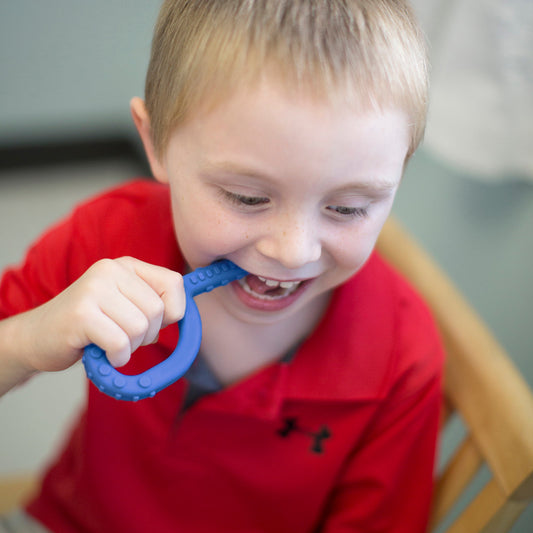 child using blue ARK grabber oral motor chew tool for sensory needs. May be NDIS funded.