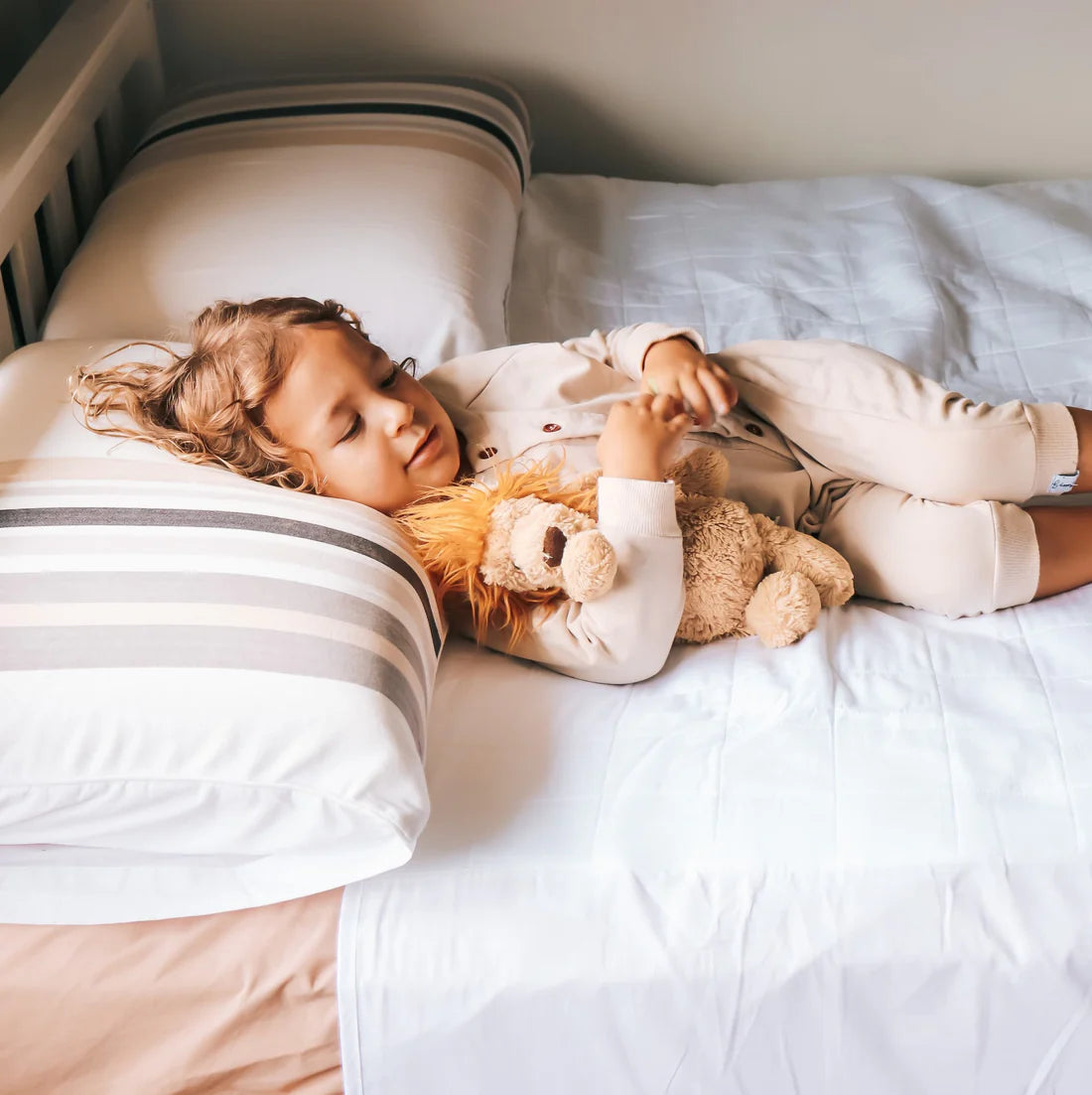 Child lying in bed with a teddy bear, holding a doll, wearing pajamas. Bedwetting Brolly Sheets - White