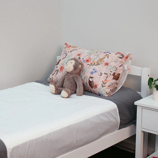 Children's bedroom with a bed featuring a monkey plush toy and floral pillow, next to a nightstand. Bedwetting Brolly Sheets - White