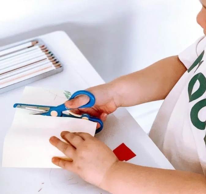 Child using blue safety scissors to cut paper, developing scissor skills and hand coordination – ideal for early fine motor development and potentially NDIS-funded